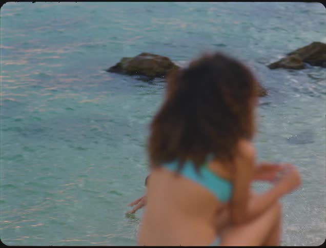 Man runs through the water while two women chat sitting at the edge of the beach