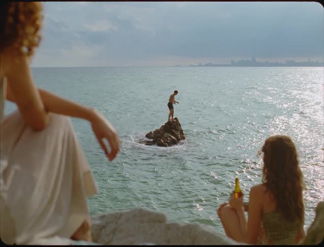 Man dives off the rock as two people watch from the shoreline
