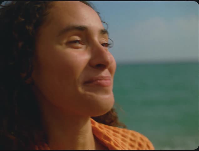 A woman laughs and smiles while standing on an ocean shore