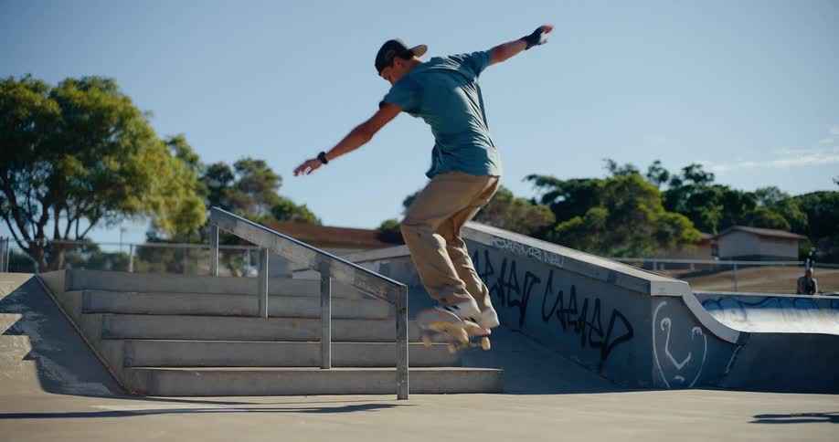 A skateboarder performs a trick grinding a graffiti covered rail in a sunny park