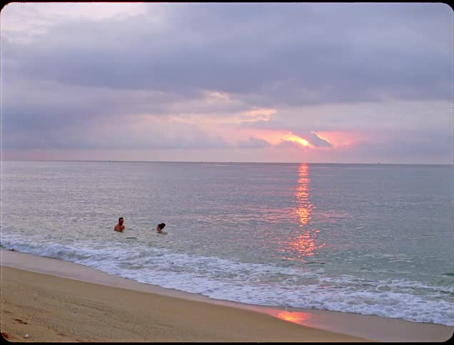 Two adults a man and a woman swim together in the ocean near the beach at sunset enjoying their time in the water