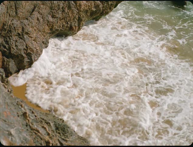 Waves crash onto a triangle shaped beach with mountains