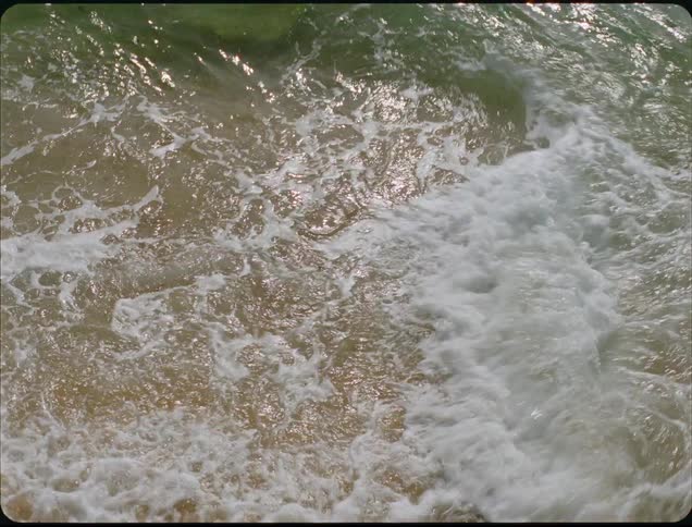 Turbulent waves crash on sand with white foam under sunlight reflections