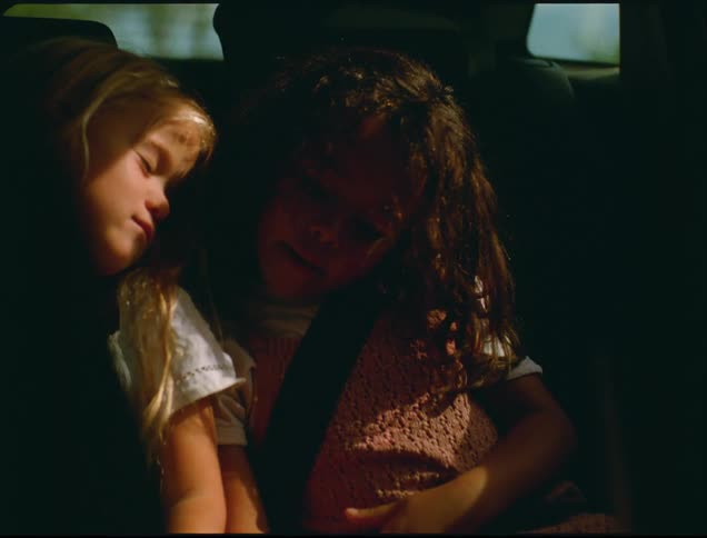 Two children are in a car with seatbelts on as they sleep