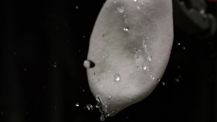 A close view shows water droplets rapidly forming beads and rolling down the surface of a light gray object against a black studio backdrop