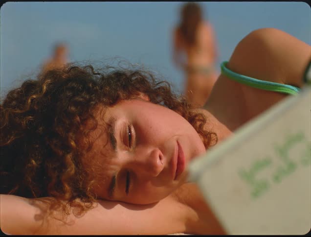 A girl laying around on the beach reading a book