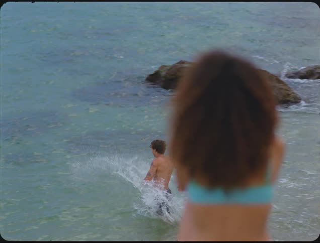 Boy runs through the shallow sea while someone watches from the shore