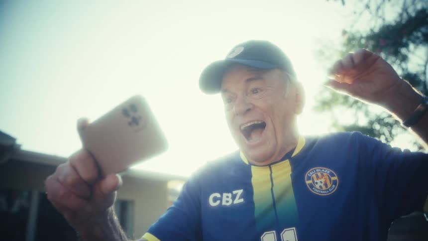 Older man smiles at phone under sunlight
