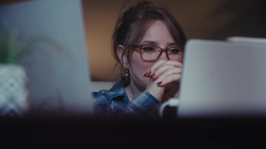The woman puts on her glasses while looking at her computer