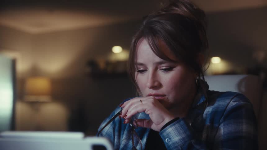Woman sitting at a desk working on a computer takes off her glasses and rubs her nose