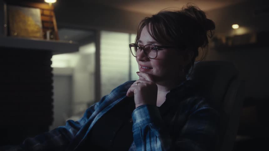 Woman wearing glasses and blue plaid shirt types on tablet with keyboard in softly lit setting