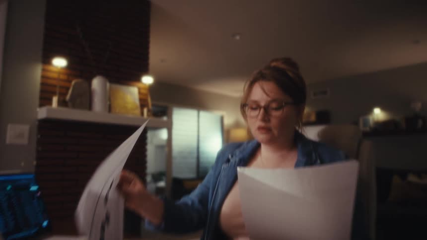 An office worker looks stressed as she looks through paperwork in front of a laptop computer