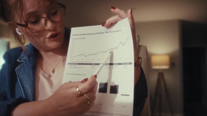A woman sitting in an office talks as she uses a pen to point at a graph on paper