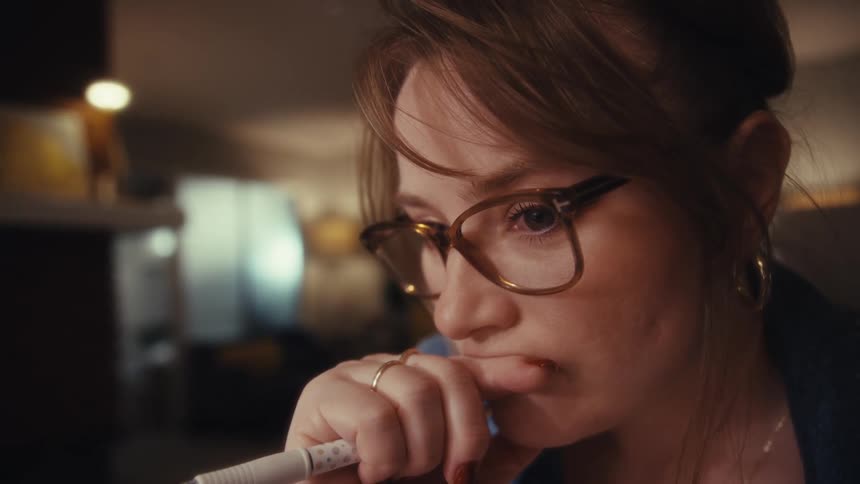Woman wearing glasses holds pen near face while looking at something offframe