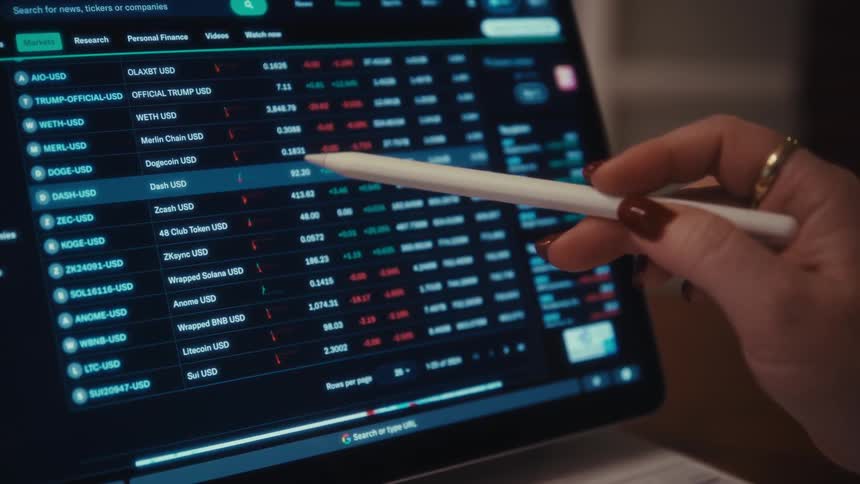 A young woman wearing glasses holds a document while looking at a computer monitor in front of her comparing figures she then removes her glasses in disappointment