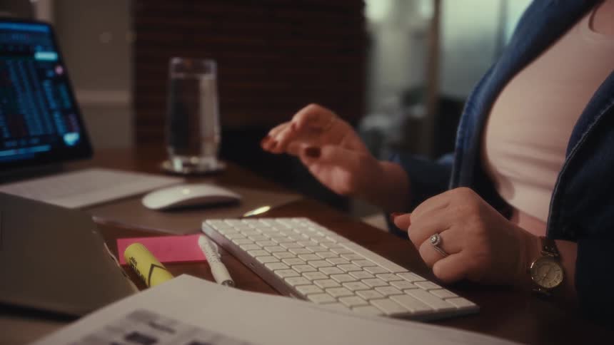 The video opens with a closeup of a person typing on a keyboard surrounded by financial papers and a calculator on a cluttered desk suggesting focused work it then shifts to a closeup of a woman in a denim jacket and glasses pausing her work to smil