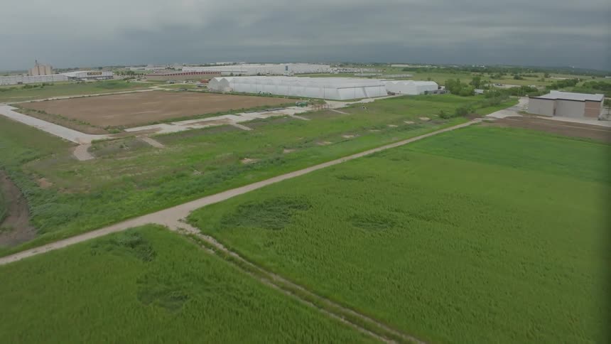 An aerial view of green fields with industrial greenhouses under an overcast sky