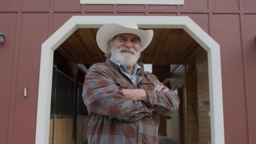 The cowboy is smiling in front of the stable