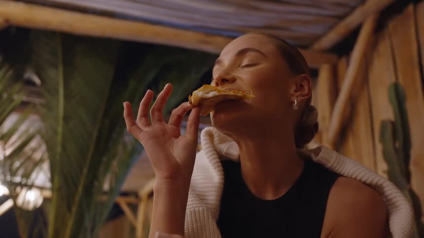 A woman enjoys a bite of food with her eyes closed in a cozy dimly lit restaurant