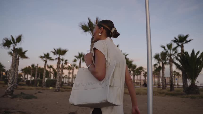 A woman carrying a large handbag is walking on a path through palm trees