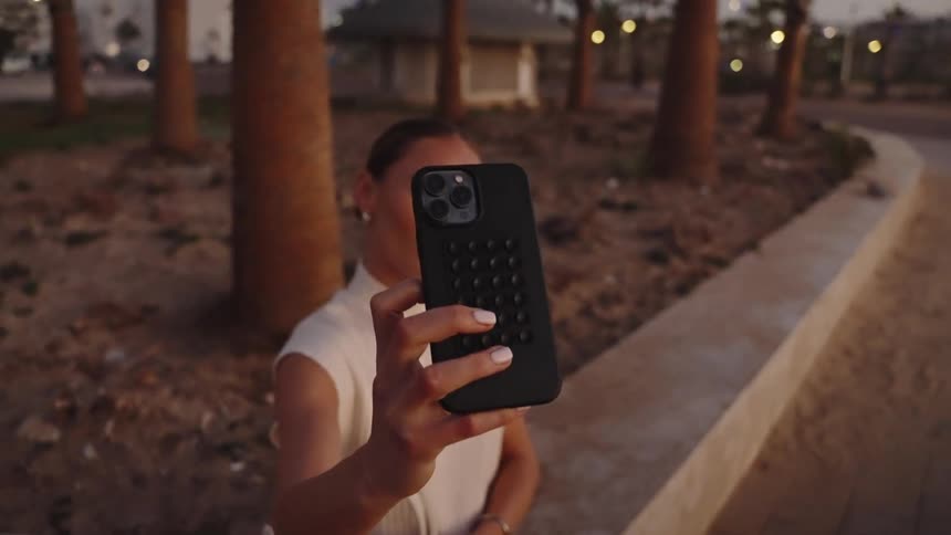 A woman is sitting outside under palm trees taking a selfie with her phone