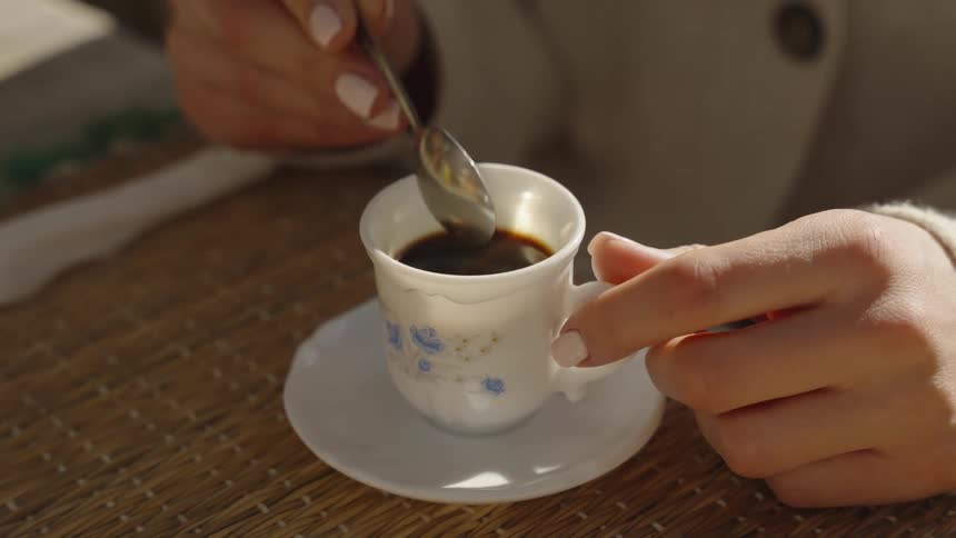 A woman sitting at a table stirs her coffee with a spoon