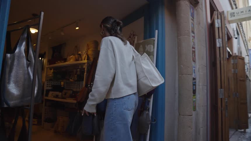 A woman carrying a white purse is entering a store that has its doors open