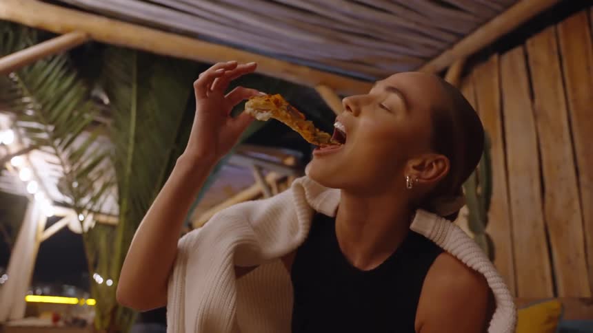 The woman is eating pizza outside