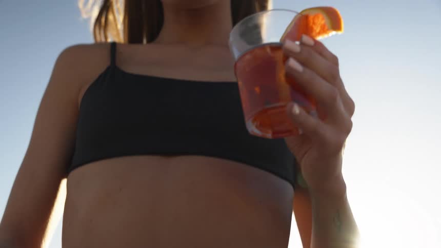 Woman holds a drink with an orange slice outdoors