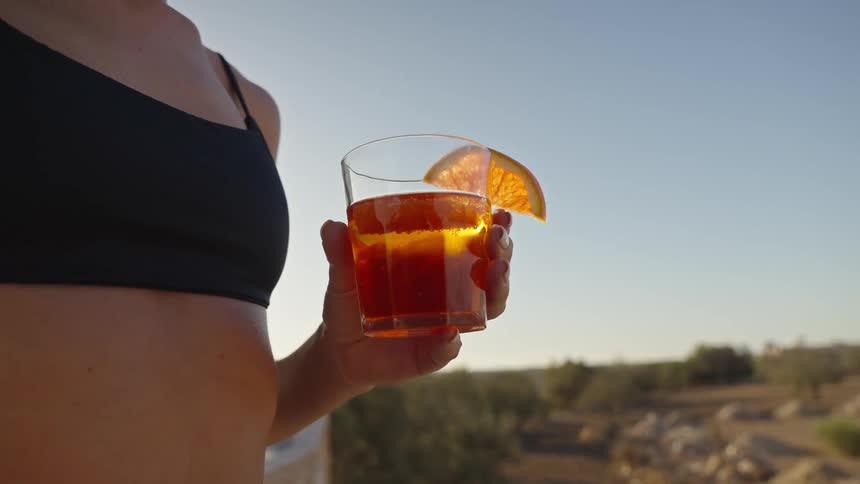 Woman stands outside holding a drink with a slice of lemon on the glass