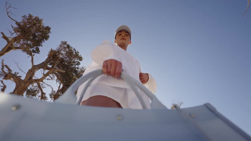 Woman in white clothing placing a silver metallic bag seen from below against a clear blue sky