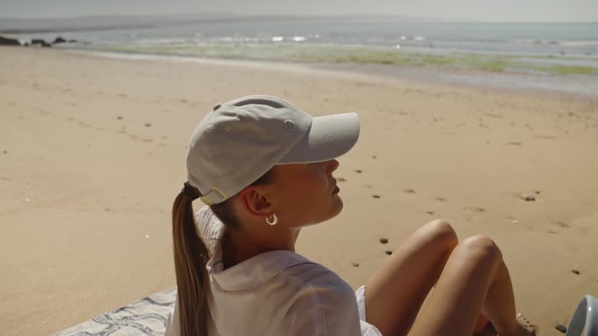 A woman rests on a towel on a sunny sandy beach overlooking the ocean