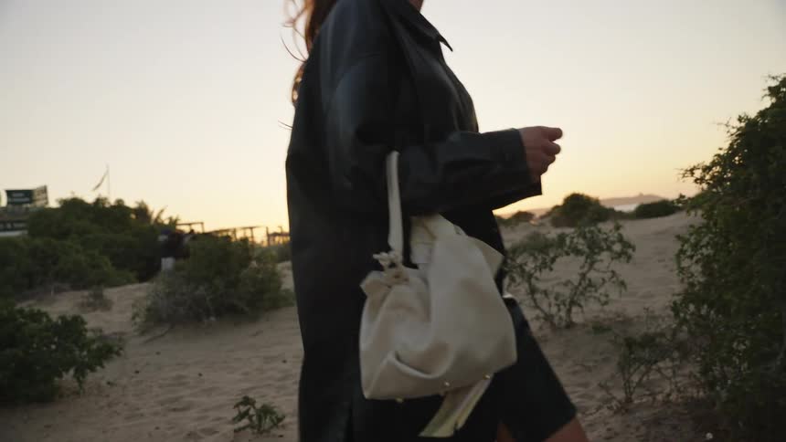 A woman carrying a handbag is walking in the sand next to a neighborhood