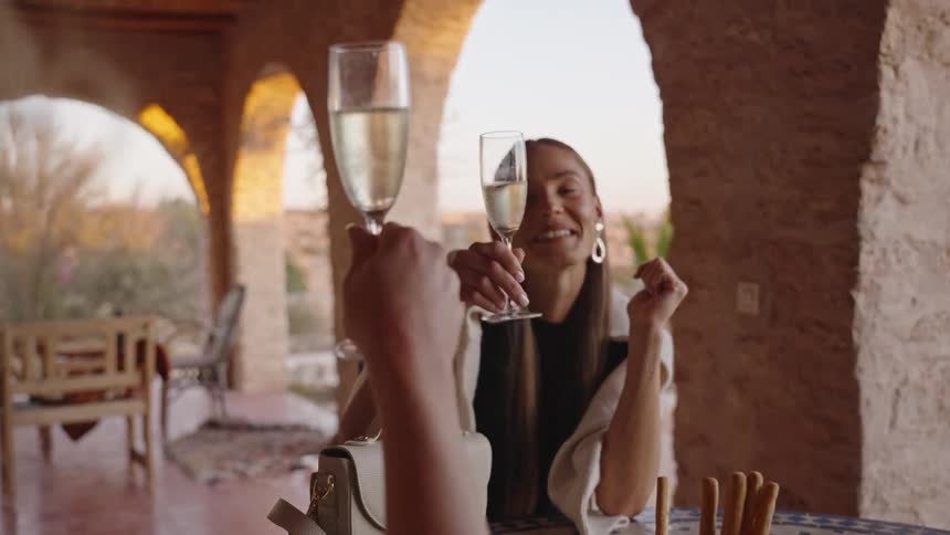 Two women toast with champagne flutes at an outdoor restaurant
