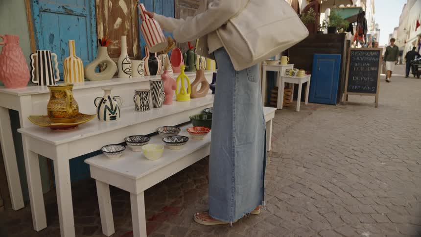 Woman looks at ceramic pieces displayed on shelves of an outdoor shop