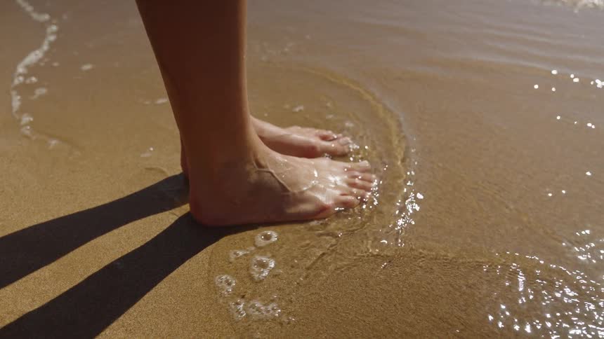 Woman standing on the beach as waves roll over her bare feet