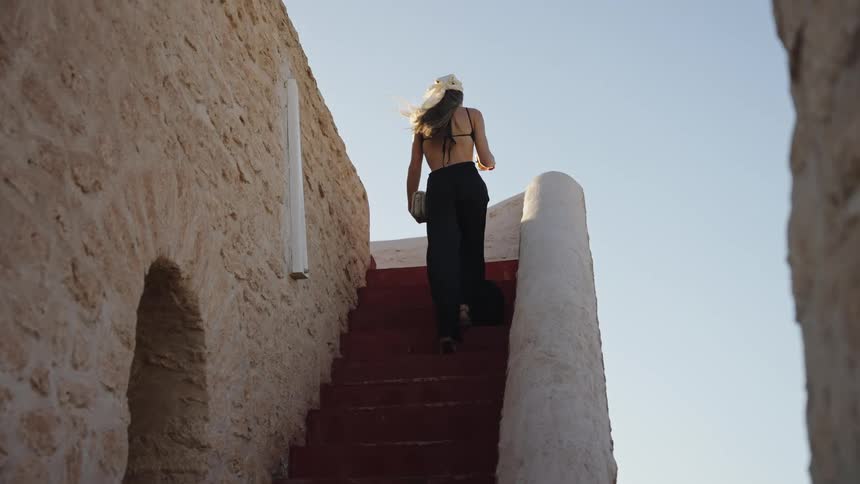 A woman carries a drink and books as she walks up an outdoor stairway