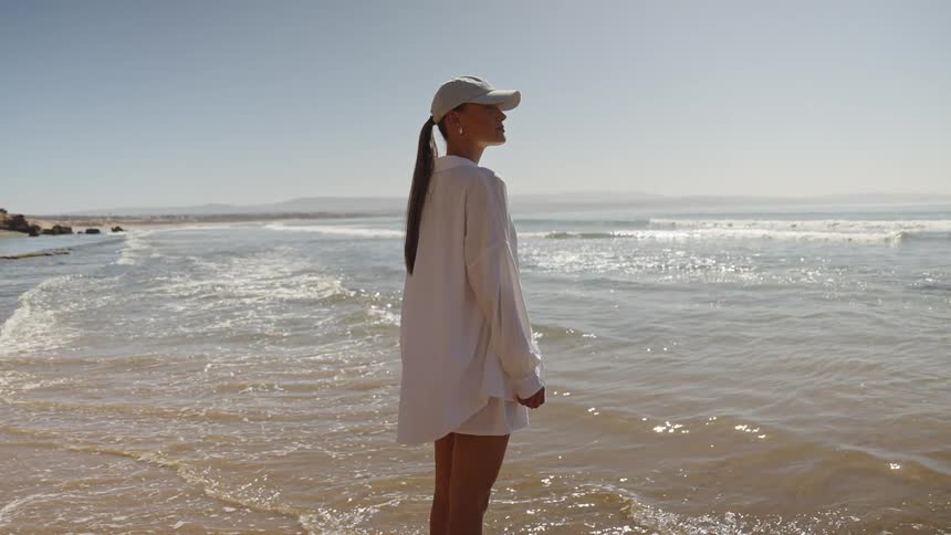 Woman standing in shallow water on the beach as waves roll into shore
