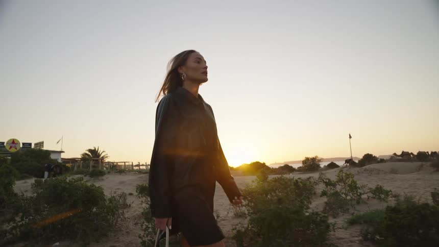 Woman walking at sunset carrying a bag in a coastal area