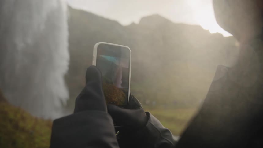 A person is using their phone to record a waterfall coming down over the side of a mountain