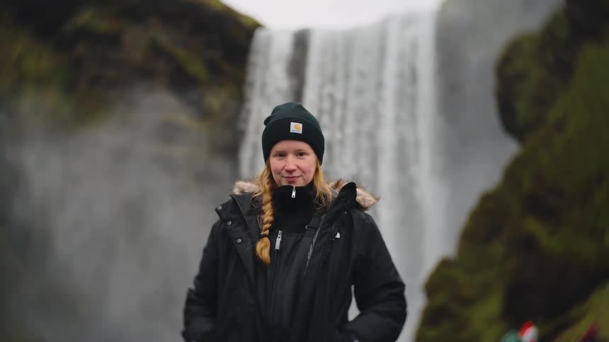A woman looks up as she stands in front of a waterfall in the mountains