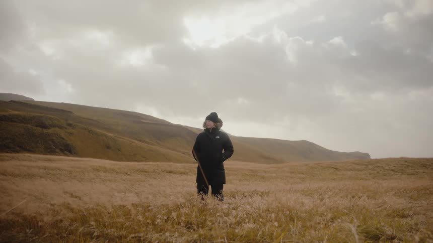 Clouds gather overhead as a person stands in a grassy field in the mountains
