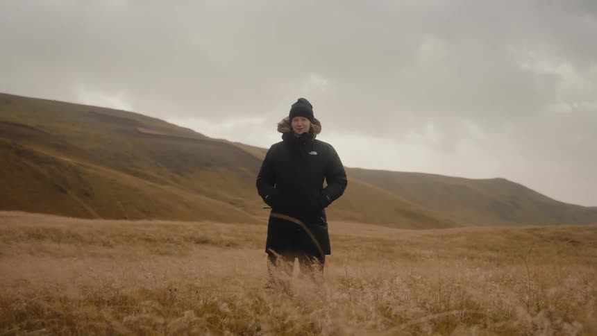 Woman in black jacket standing in field of wheat grass in the countryside on a windy day