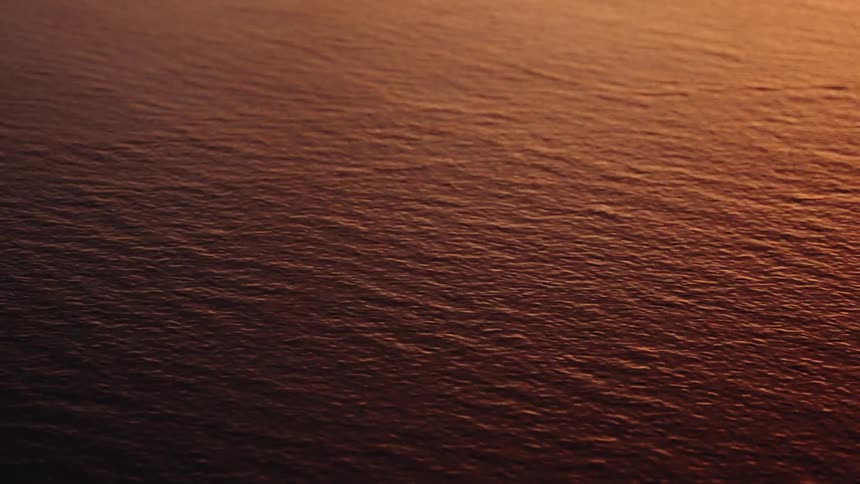 A static closeup view captures the textured surface of water gently rippling under warm golden light