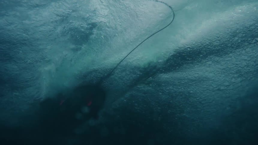 An abstract underwater shot begins with the distorted surface showing a surfer passing over and then transitions to a dark turquoise blue depth