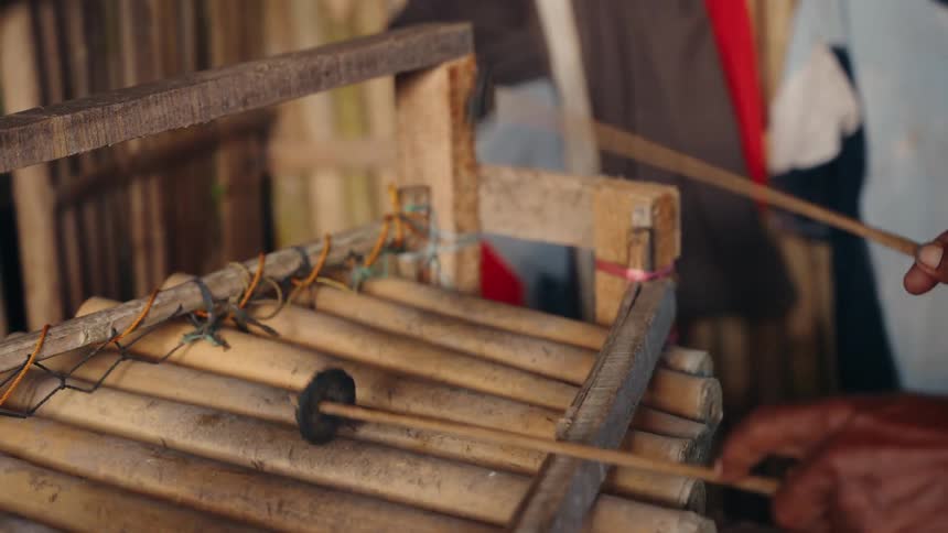 The video shows a closeup of a person playing a traditional wooden or bamboo percussion instrument possibly a form of xylophone or gamelan componentthe players hand quickly strikes the bamboo bars with two slender wooden mallets to produce sound v