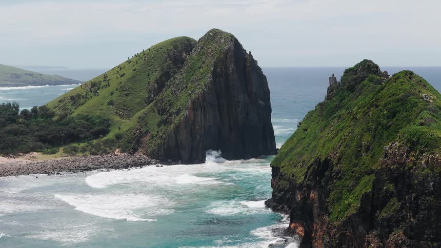 Aerial view of green cliffs and a rocky bay with turquoise waves under a clear sky