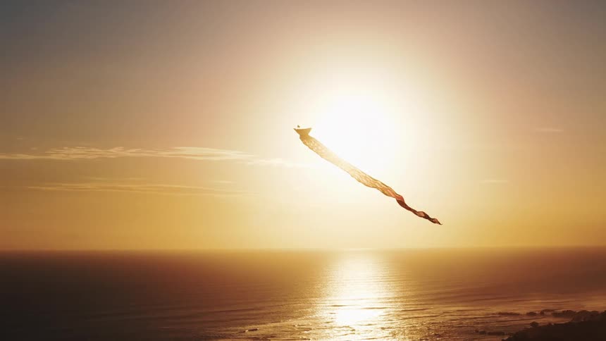 Kite flies along the coast as light from the setting sun reflects on the water