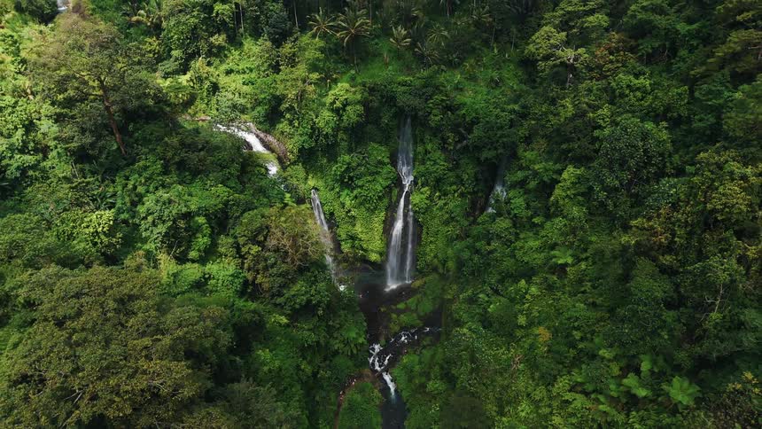 Aerial view of a thin waterfall flowing through a lush green ravine with nearby rice terraces