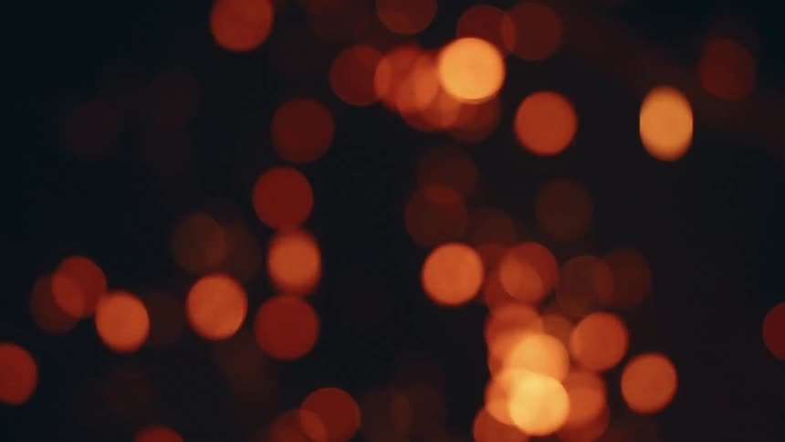 The video is a dark abstract shot focusing on bokeh effects which are circular outoffocus highlightsthe orange and red glowing circles appear to intensify and then dissipate possibly simulating embers or lights against a black background